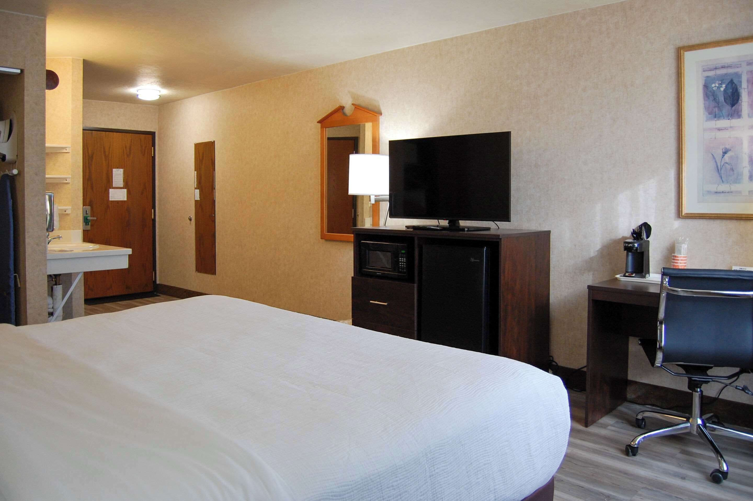 A hotel room with a large bed, a desk with a computer, a television, a microwave, and a small cabinet.