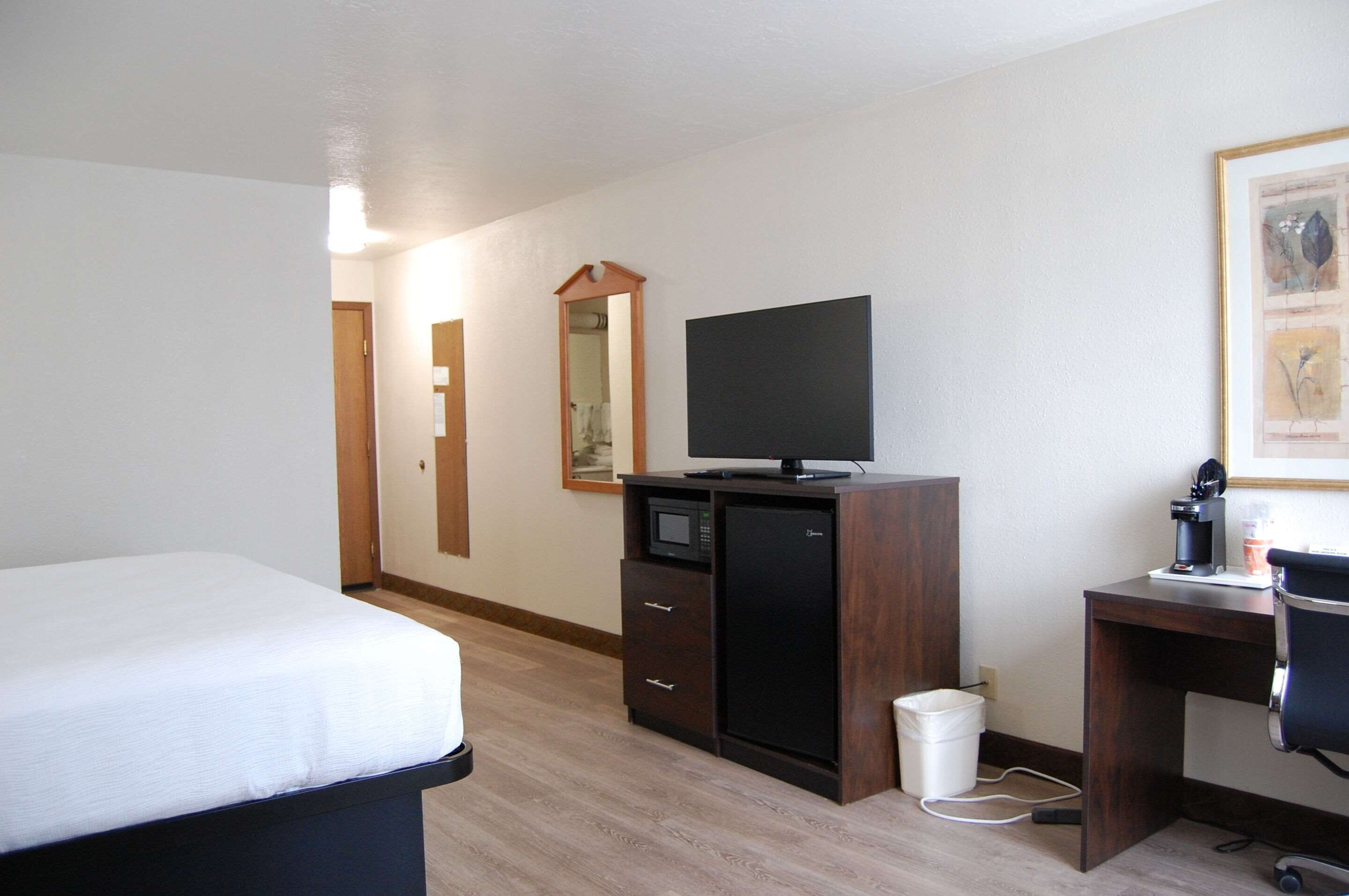 A hotel room with a bed, a desk with a computer, a television, a microwave, and a small trash bin.