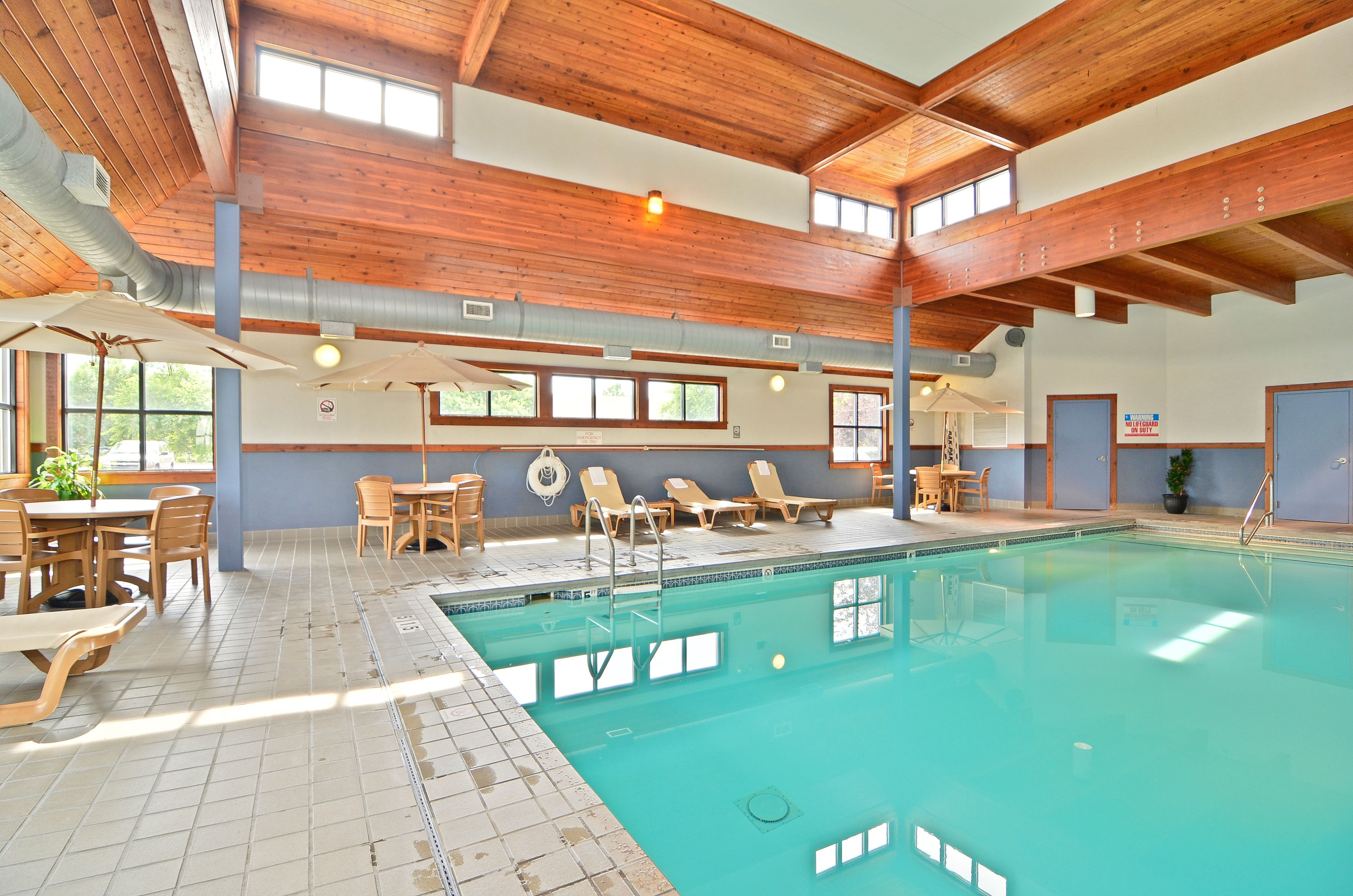 An indoor swimming pool with wooden beams, sunlit windows, and lounge chairs.