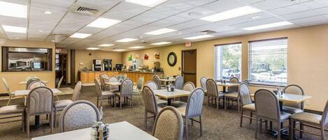 A dining area with multiple tables and chairs, a kitchen area with appliances, and large windows providing natural light.