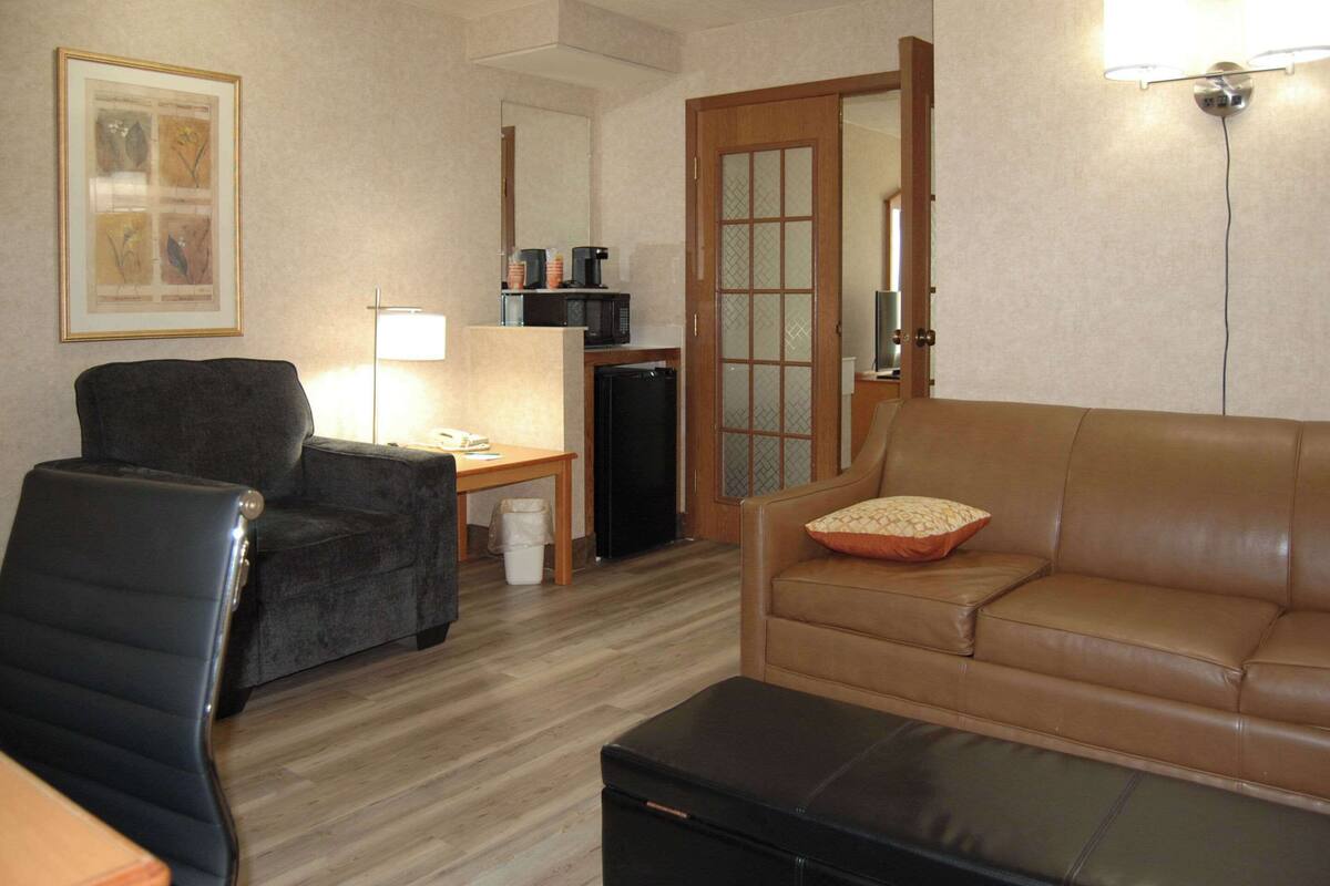 A living room with a black leather chair, a brown leather sofa, a small table with a lamp, and a microwave on a shelf.