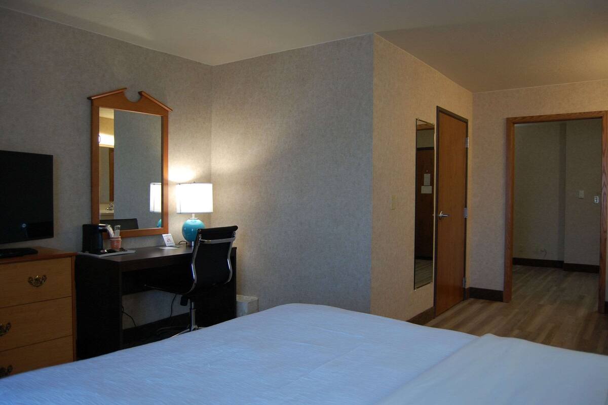 A hotel room with a bed, a desk with a chair, a desk lamp, a TV, and a mirror.