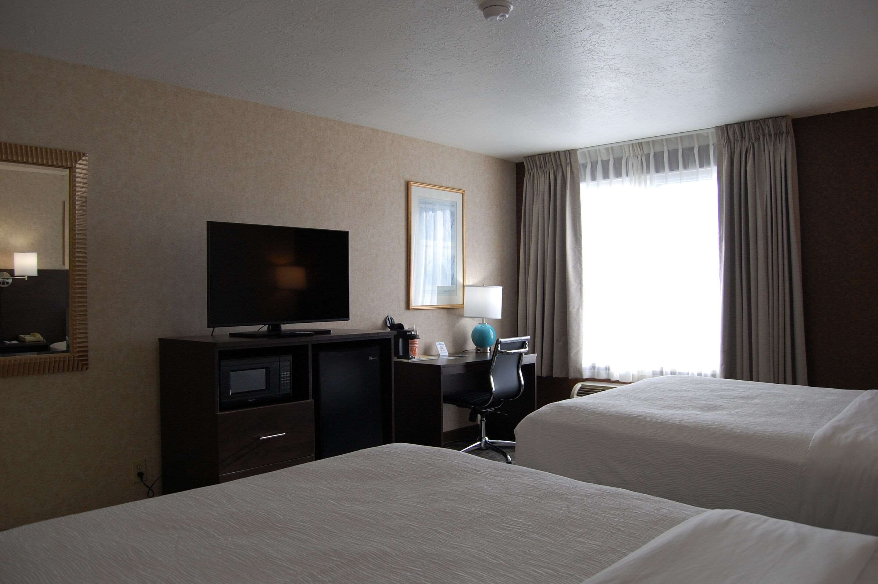 Habitación de hotel con dos camas, televisión, escritorio con lámpara y ventana con cortinas.