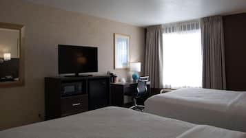 Habitación de hotel con dos camas, televisión, escritorio con lámpara y ventana con cortinas.