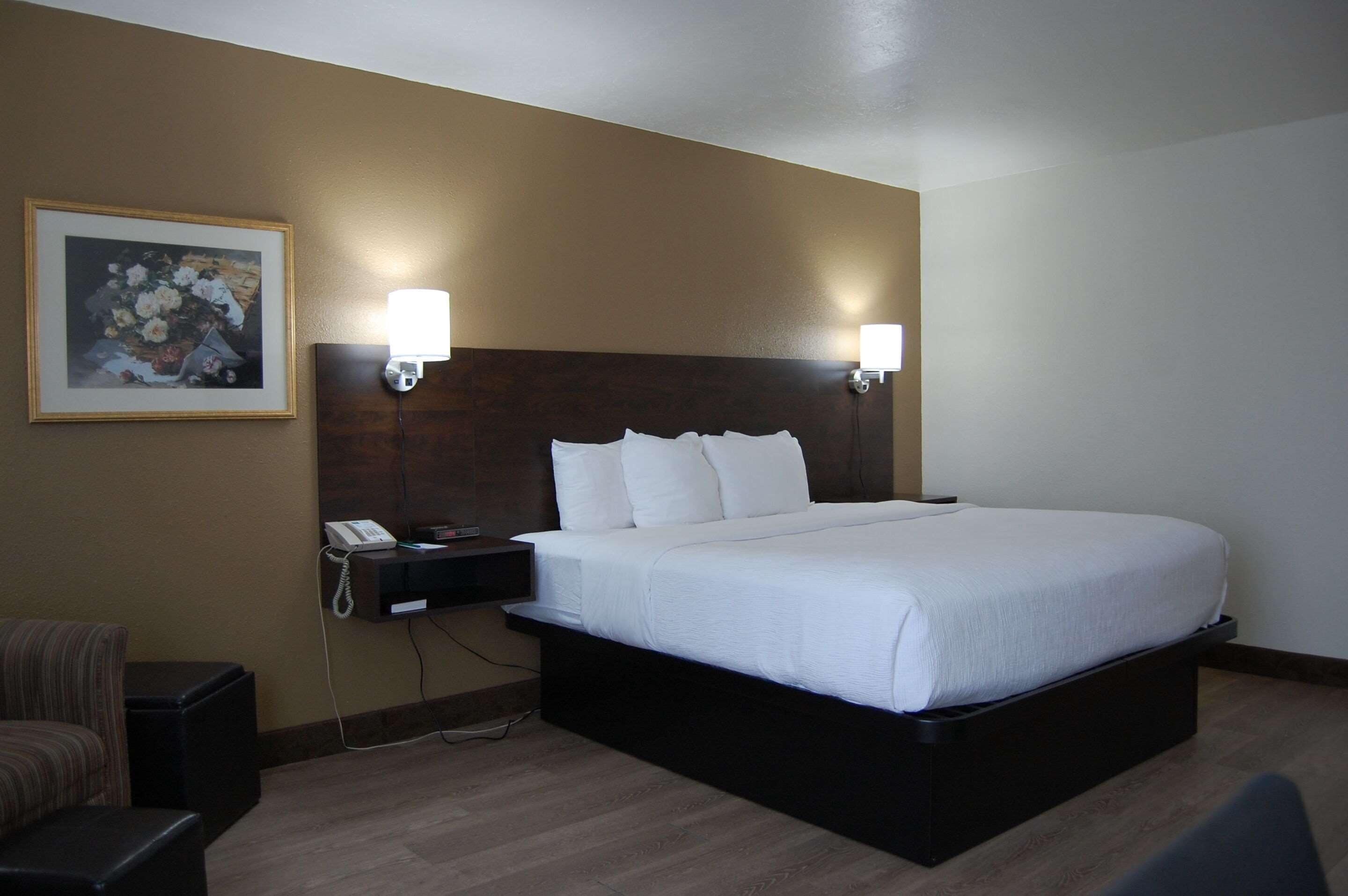 A hotel room with a large bed, two bedside lamps, a phone on a nightstand, and a framed picture on the wall.