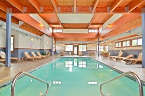 Une piscine intérieure avec des poutres en bois, des chaises longues et des tables.