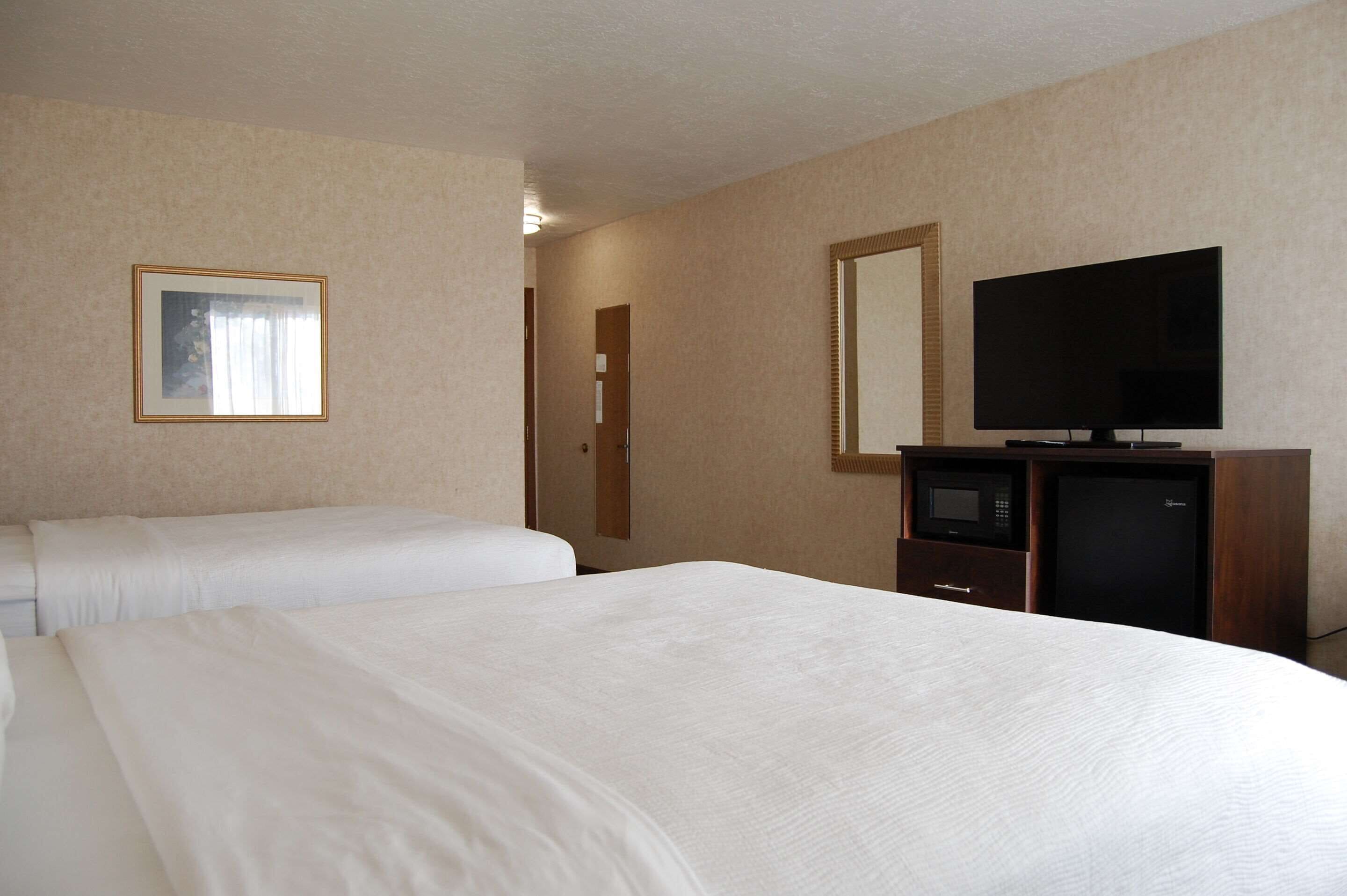 A hotel room with two beds, a television, a microwave, and a door leading to another room.