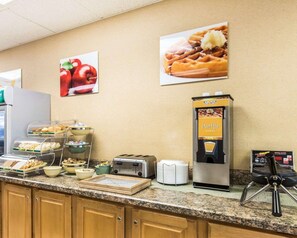 A breakfast bar with a waffle maker, toaster, and various food items.