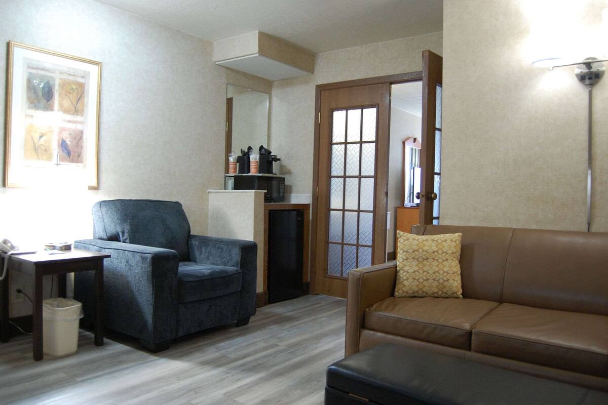 A living room with a dark blue armchair, a brown leather sofa, a small table with a telephone, and a trash bin.