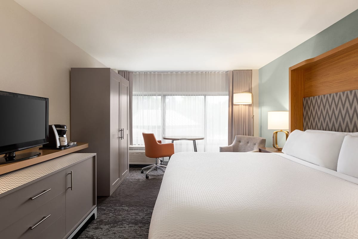 A hotel room with a large bed, a television, a desk with a lamp, and a chair.