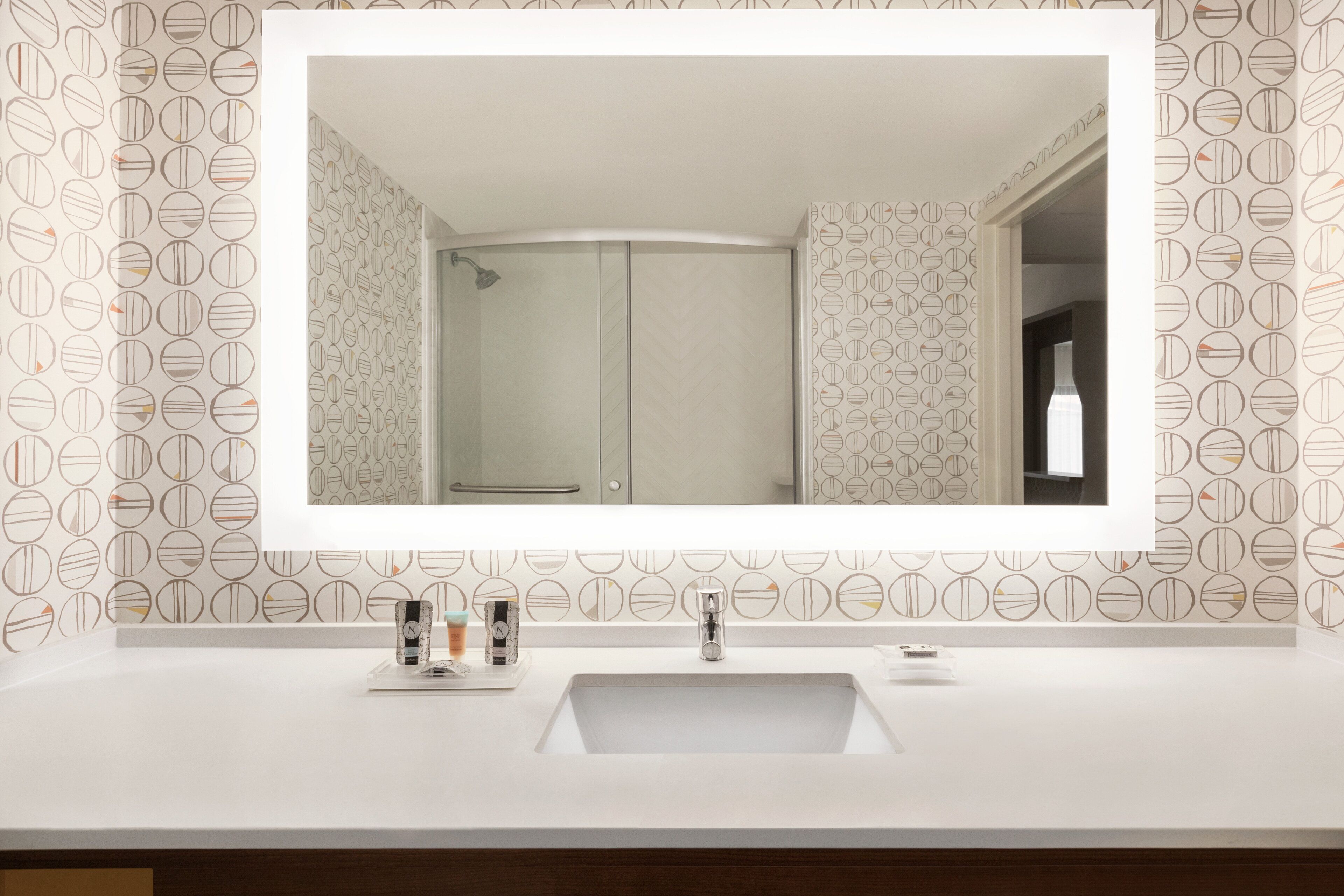 A bathroom with a large mirror, a sink, and a shower.