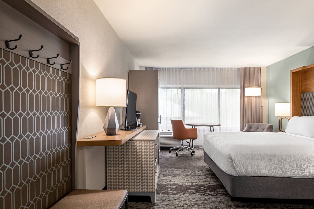 A hotel room with a bed, desk, chair, and a TV.