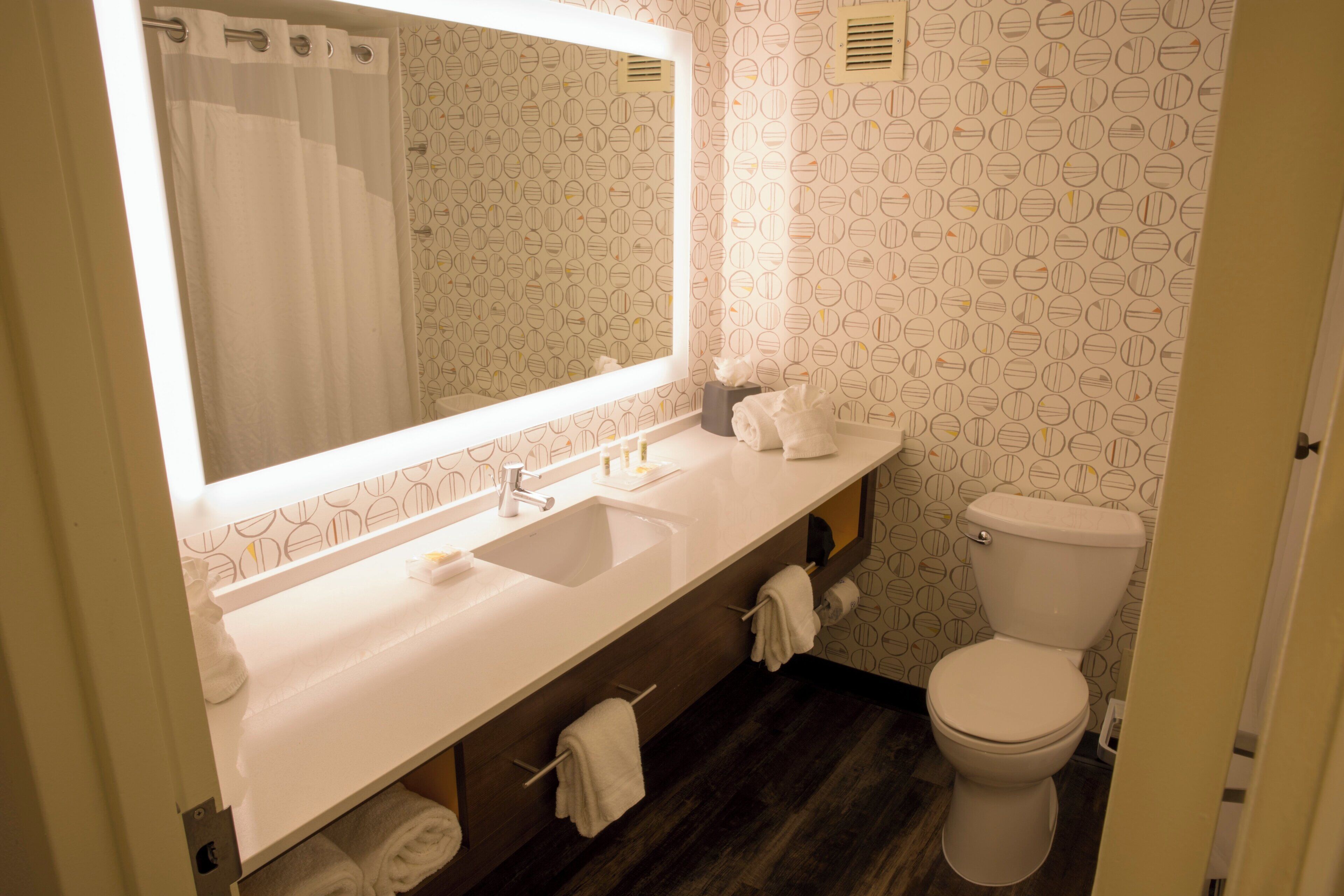 Un baño con un espejo grande, dos lavamanos, un inodoro y una cortina de ducha.