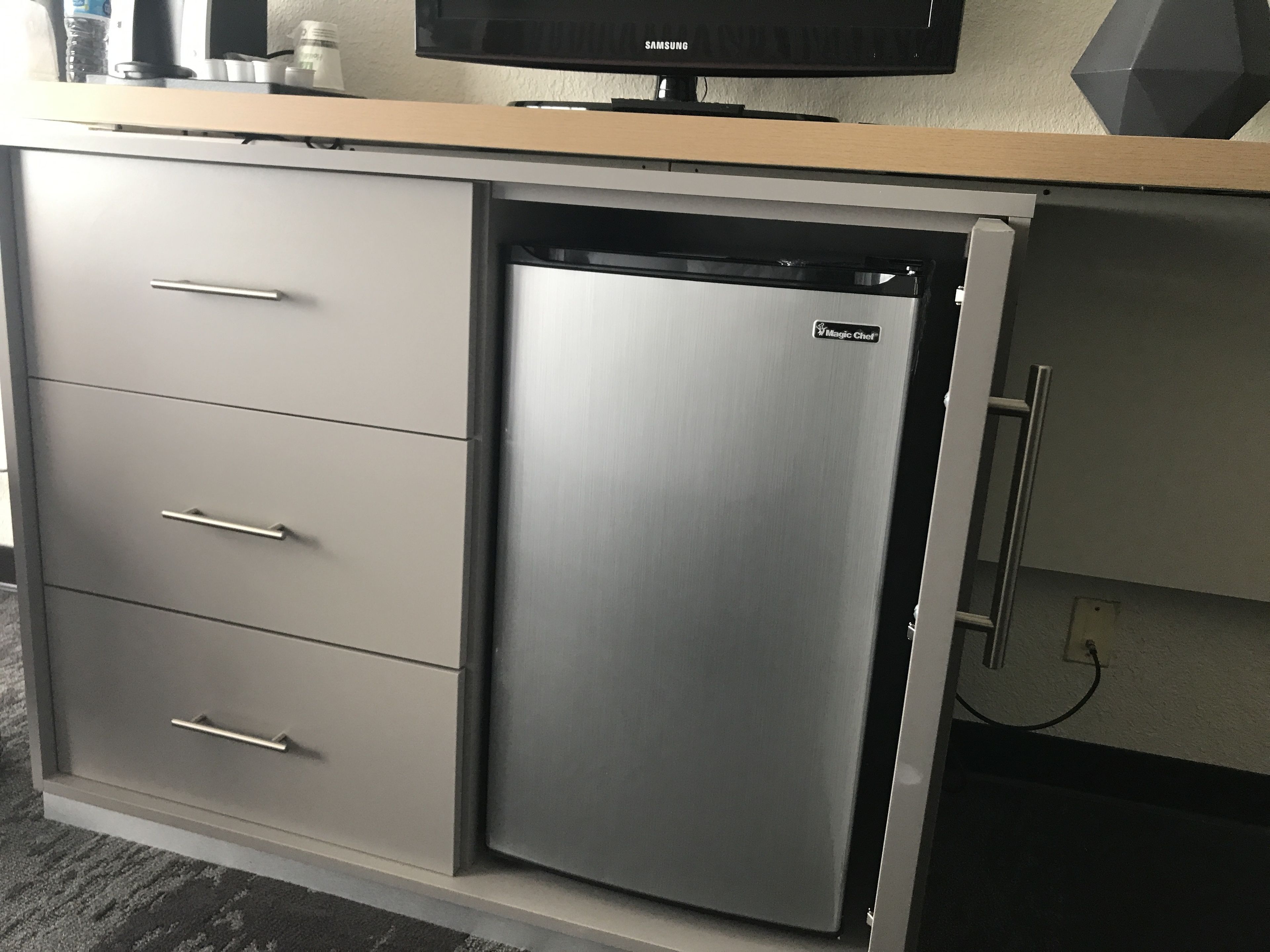 A compact kitchen with a built-in refrigerator, a microwave, and a flat-screen TV.