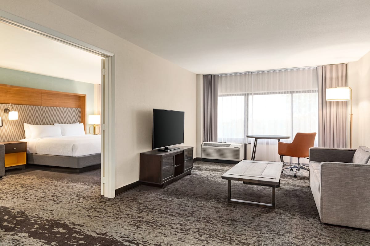 A hotel room with a bed, a TV, a desk, a chair, and a sofa.