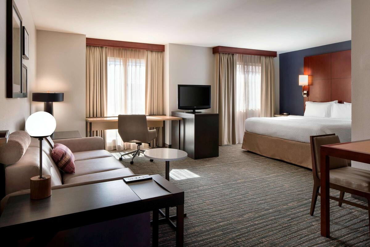 Una habitación de hotel con cama, escritorio, televisor, sofá y silla.