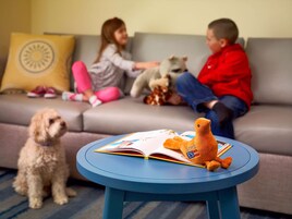 Uma sala de estar com uma mesa redonda azul, um sofá e duas crianças brincando com brinquedos.