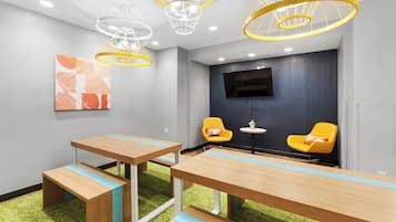 A modern meeting room with wooden tables, yellow chairs, a flat-screen TV, and unique ceiling lights.