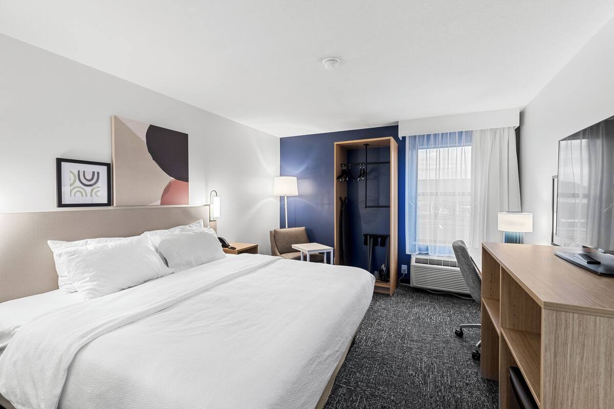 A hotel room with a large bed, a desk, a chair, a small table, and a wardrobe.