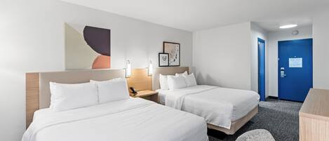 A hotel room with two beds, a desk, a chair, a blue door, and a wall with artwork.