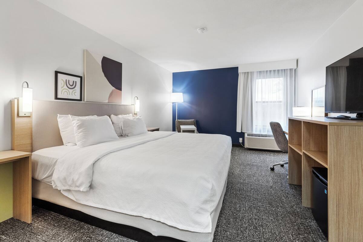 A hotel room with a large bed, a desk, a chair, a TV, and a window with curtains.