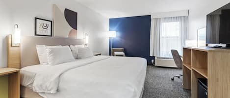 Habitación de hotel con una cama grande, un escritorio, una silla, un televisor y una ventana con cortinas.