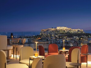 Une terrasse sur le toit, aménagée avec des sièges et des tables, d’où l’on peut admirer un panorama sur la ville et un bâtiment historique.