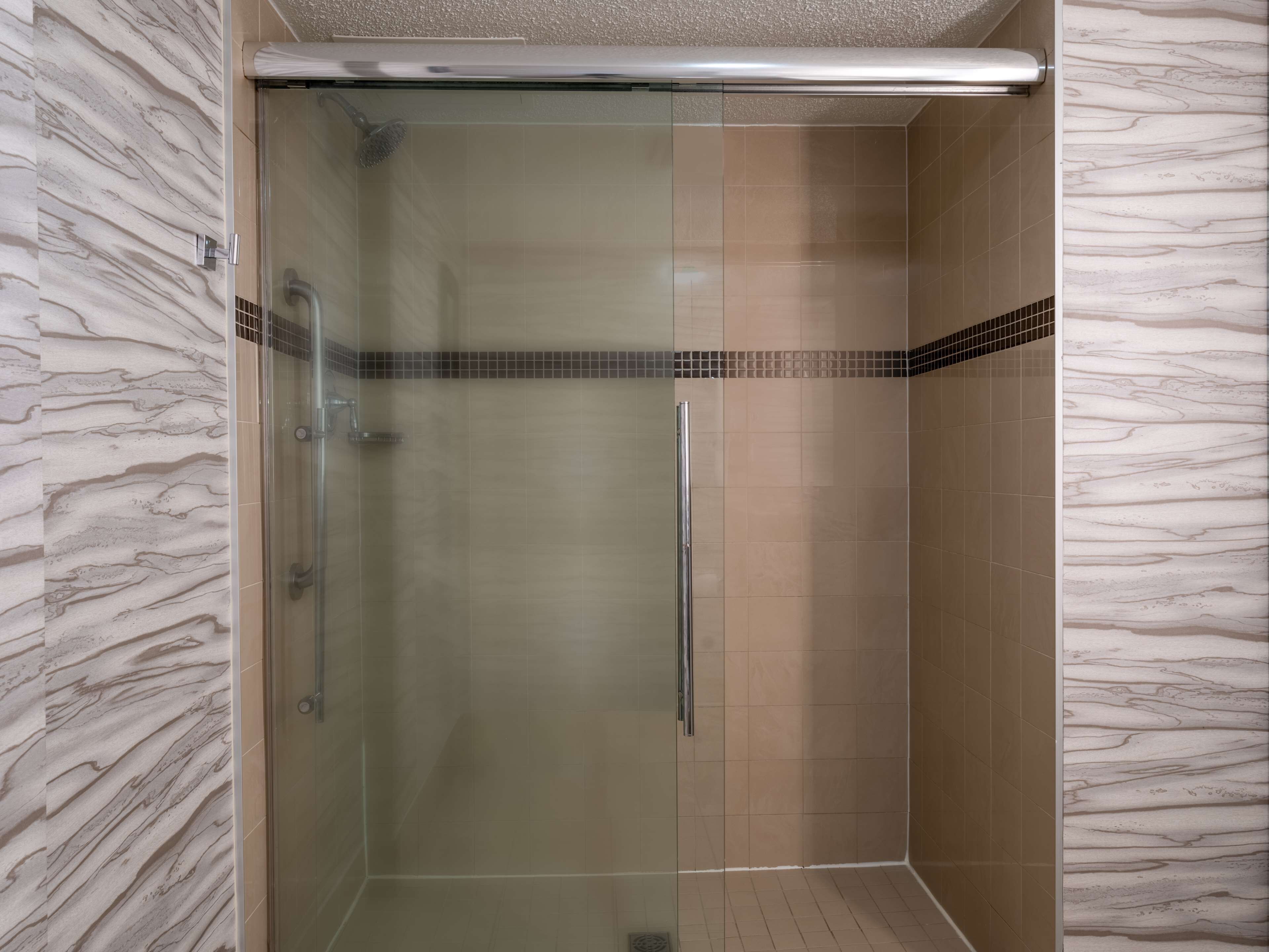 A glass-enclosed shower stall with a tiled floor and walls, a showerhead, and a handheld shower attachment.