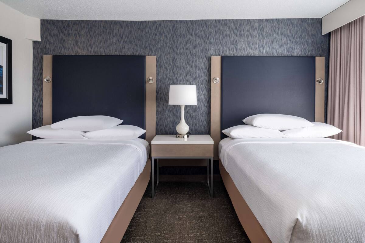 A hotel room with two beds, a nightstand with a lamp, and a textured wall.