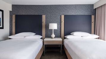 Una habitación de hotel con dos camas, una mesita de noche con lámpara y una pared con textura.