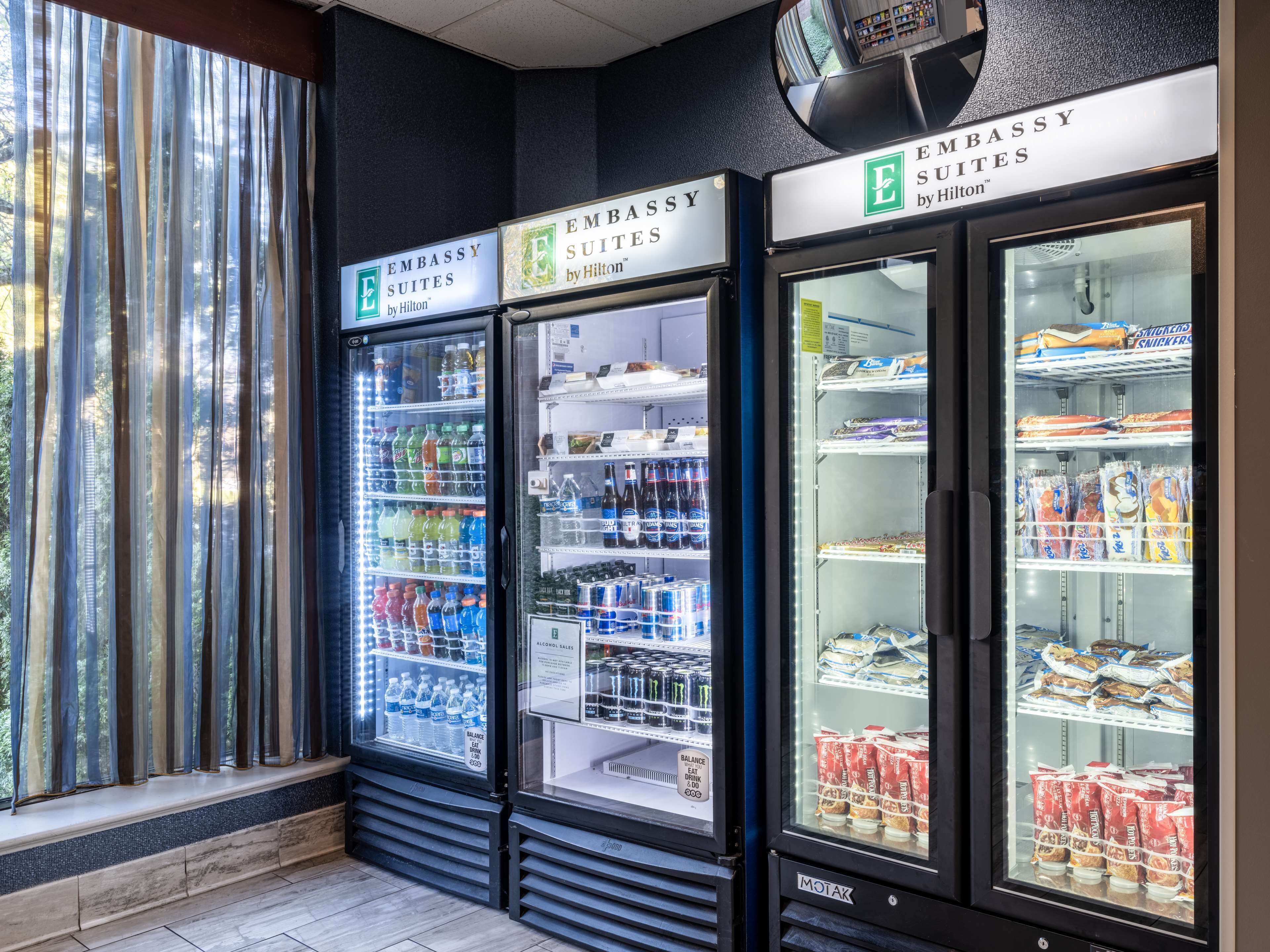 Three refrigerated display cases labeled 'Embassy Suites by Hilton' containing beverages, snacks, and packaged foods.