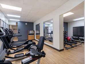 Un gimnasio con cintas de correr, bicicletas estáticas y pesas sueltas.