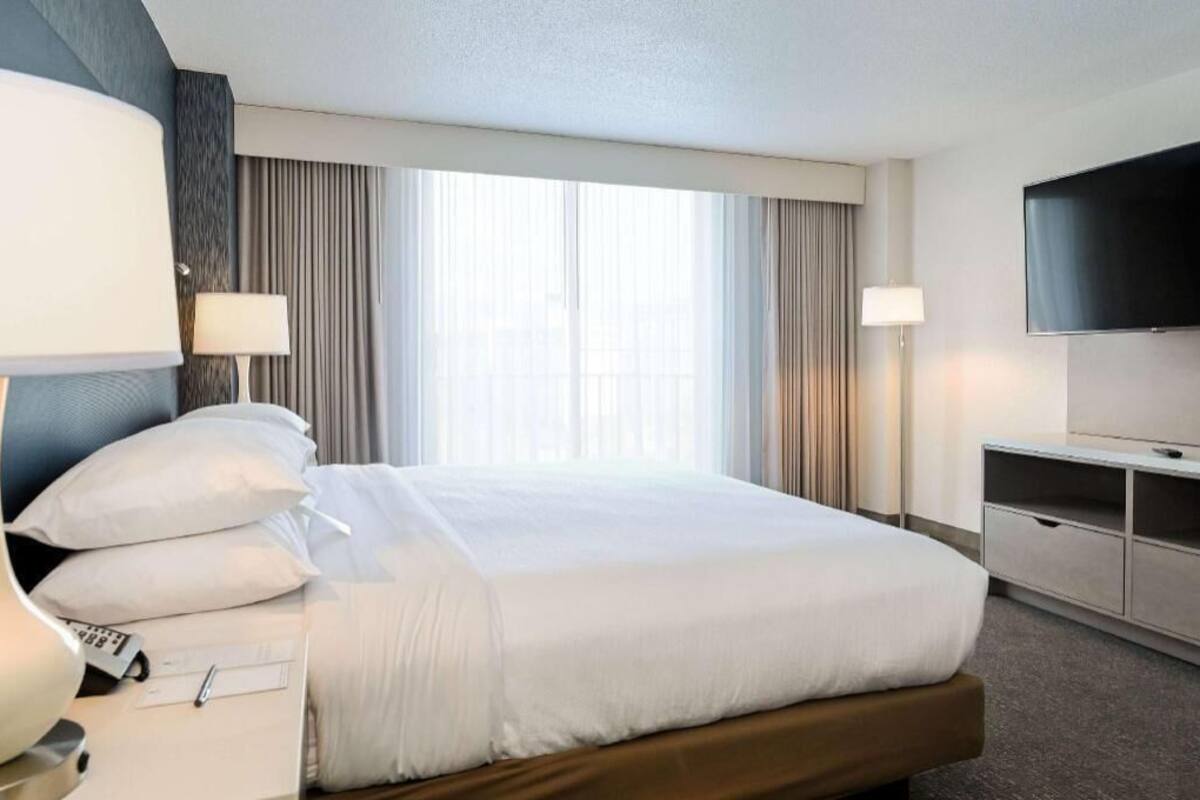 A hotel room with a bed, bedside lamps, a TV, and a window with curtains.