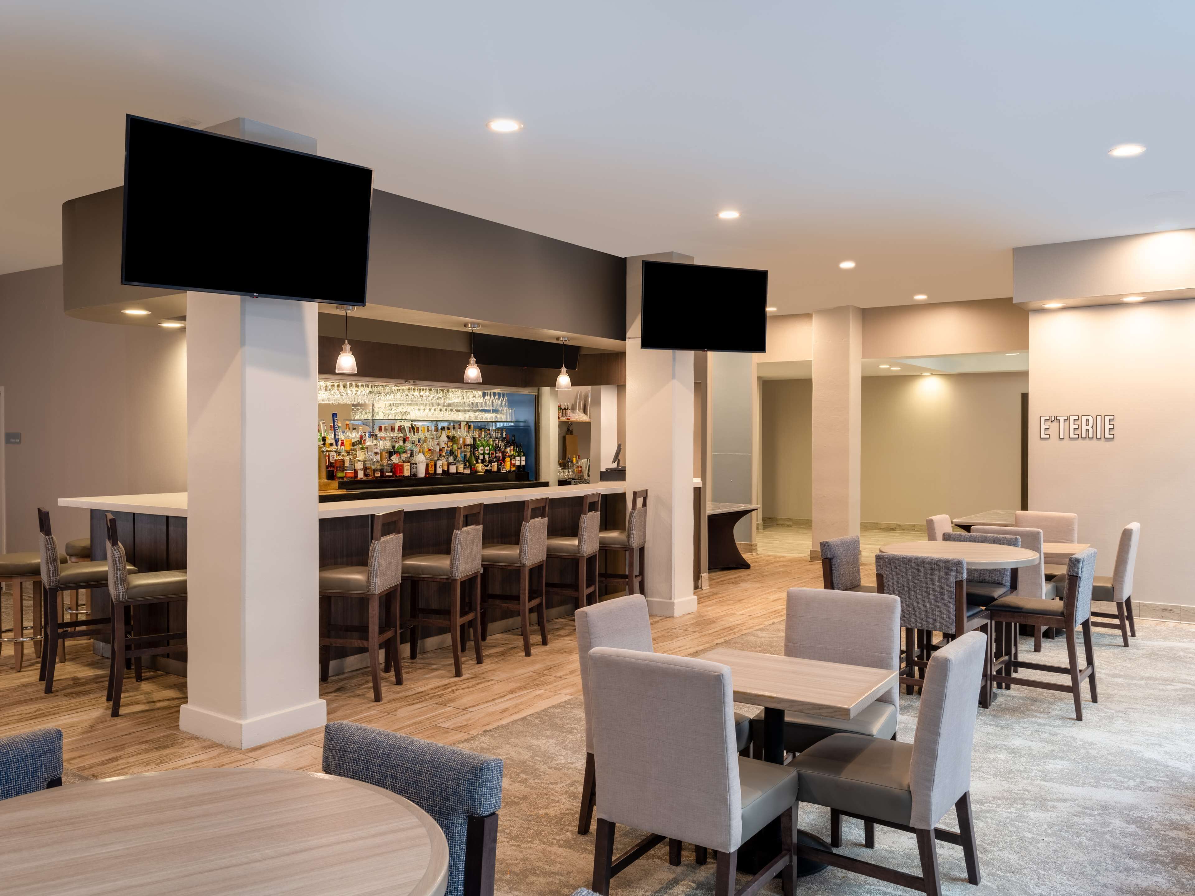 A modern bar area with multiple seating options, including bar stools and tables, and a well-lit interior with recessed lighting.