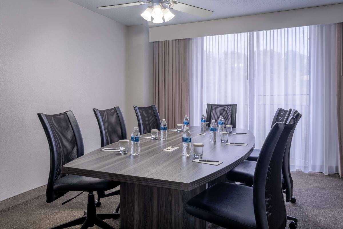 A conference room with a large table, black chairs, water bottles, and a ceiling fan.