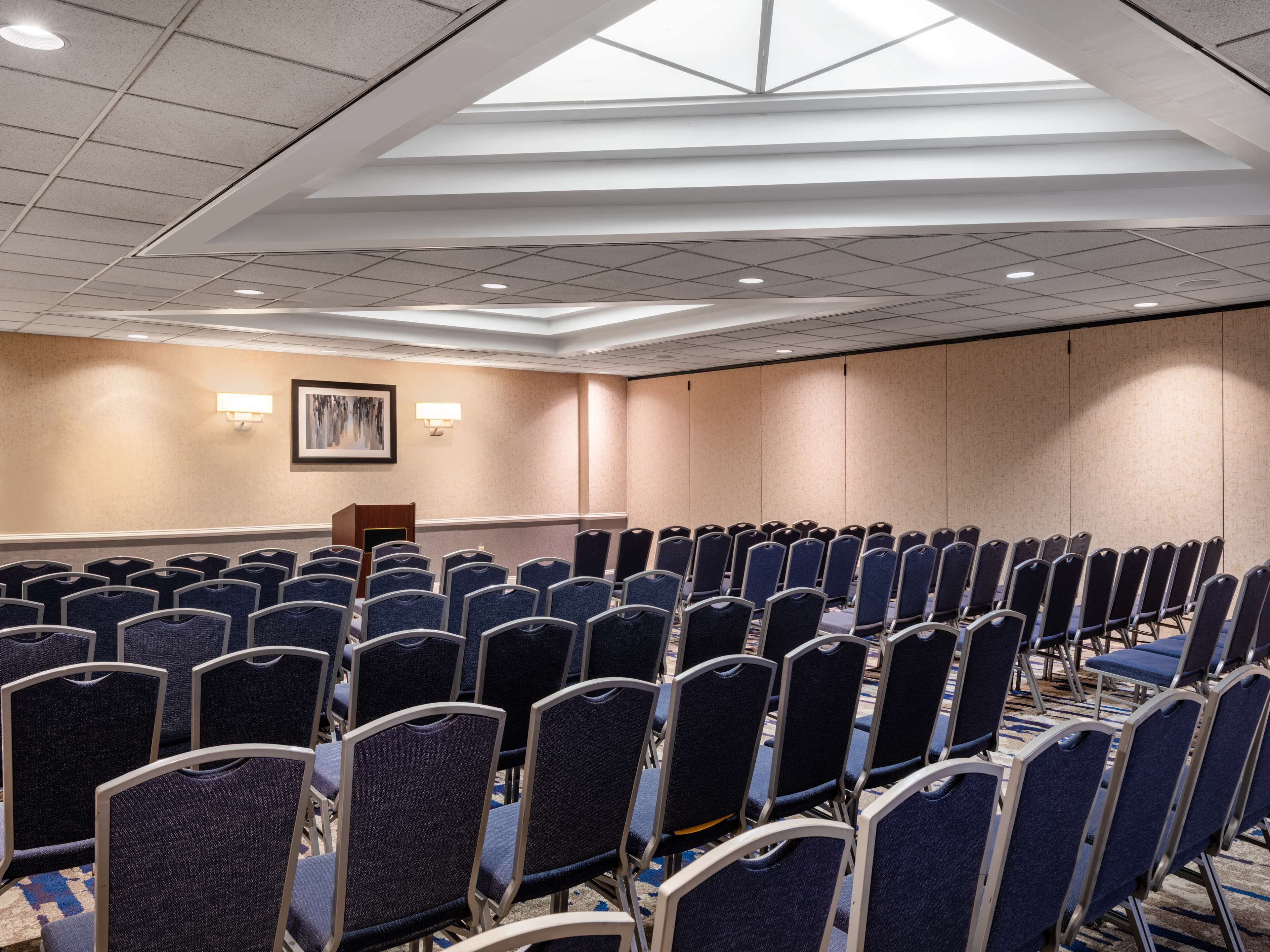 Une salle de conférence avec des rangées de chaises, un pupitre et un plafond vitré.