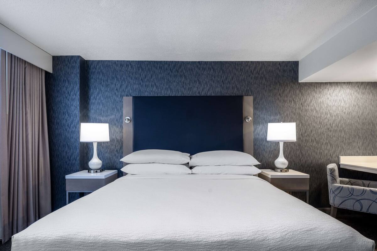 A hotel room with a large bed, two bedside tables with lamps, a chair, and a desk.