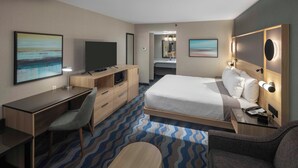 A hotel room with a bed, desk, chair, and a TV.