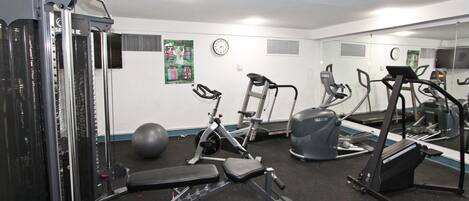 Un gimnasio con diverso equipo de ejercicio, incluyendo una caminadora, una máquina elíptica y máquinas de pesas.