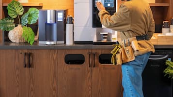 A kitchen area with wooden cabinets, a water dispenser, a coffee machine, and a recycling bin.