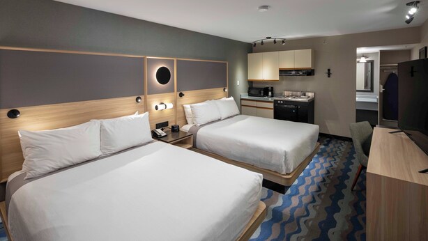 A hotel room with two beds, a desk, a kitchenette, and a bathroom.