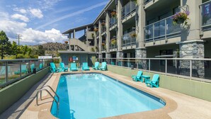A swimming pool with blue chairs and flower baskets, surrounded by a building with balconies and stone pillars.