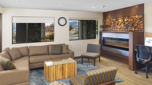 A modern lounge area with a sectional sofa, a patterned armchair, a wooden coffee table, and a fireplace. - Accent Inns Kamloops (Kamloops)