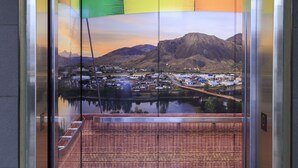 An elevator interior with a view of a town and mountains through a glass wall. - Accent Inns Kamloops (Kamloops)