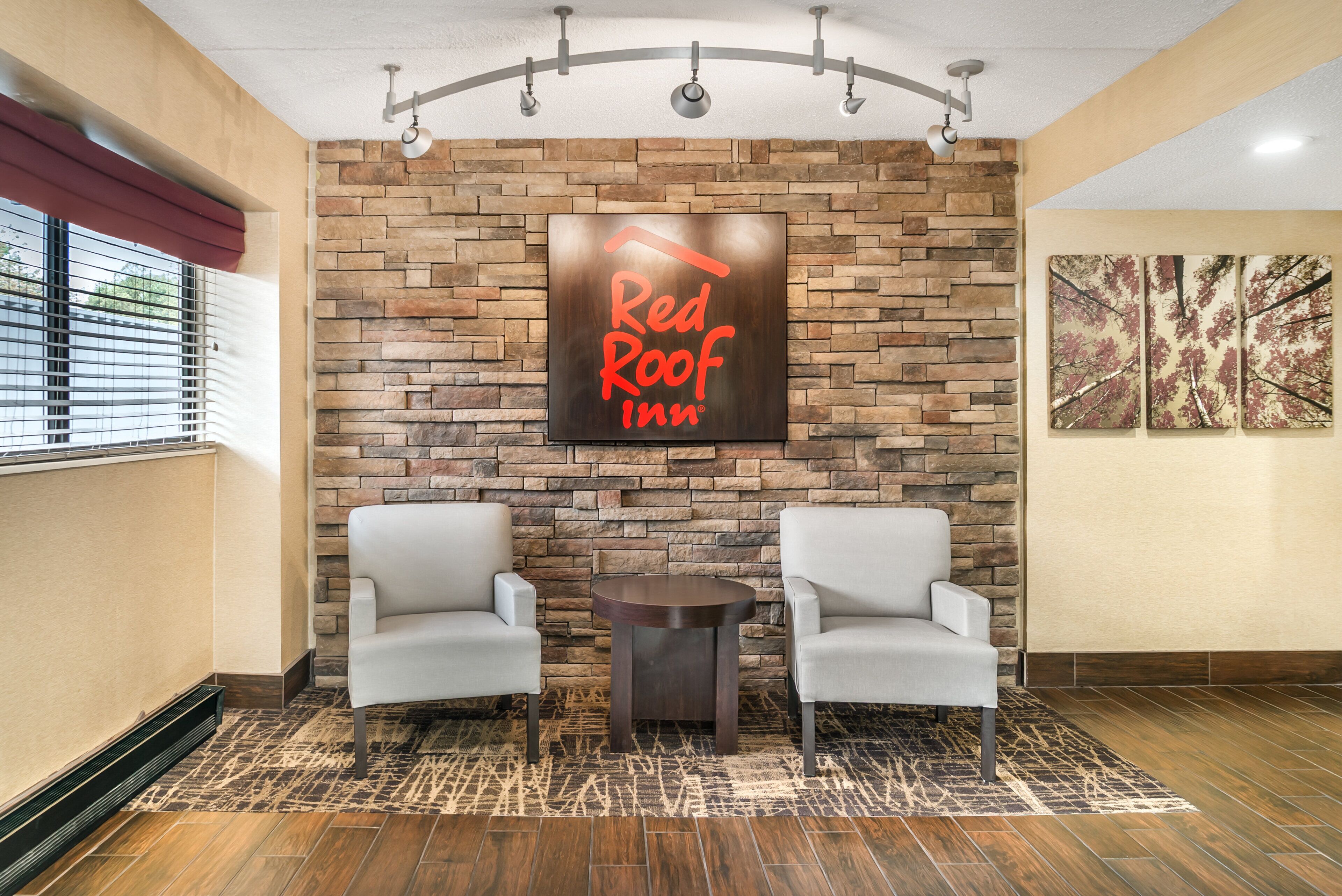 A Red Roof Inn lobby with a stone wall, two armchairs, a small table, and a ceiling fan.