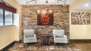 A Red Roof Inn lobby with a stone wall, two armchairs, a small table, and a ceiling fan.