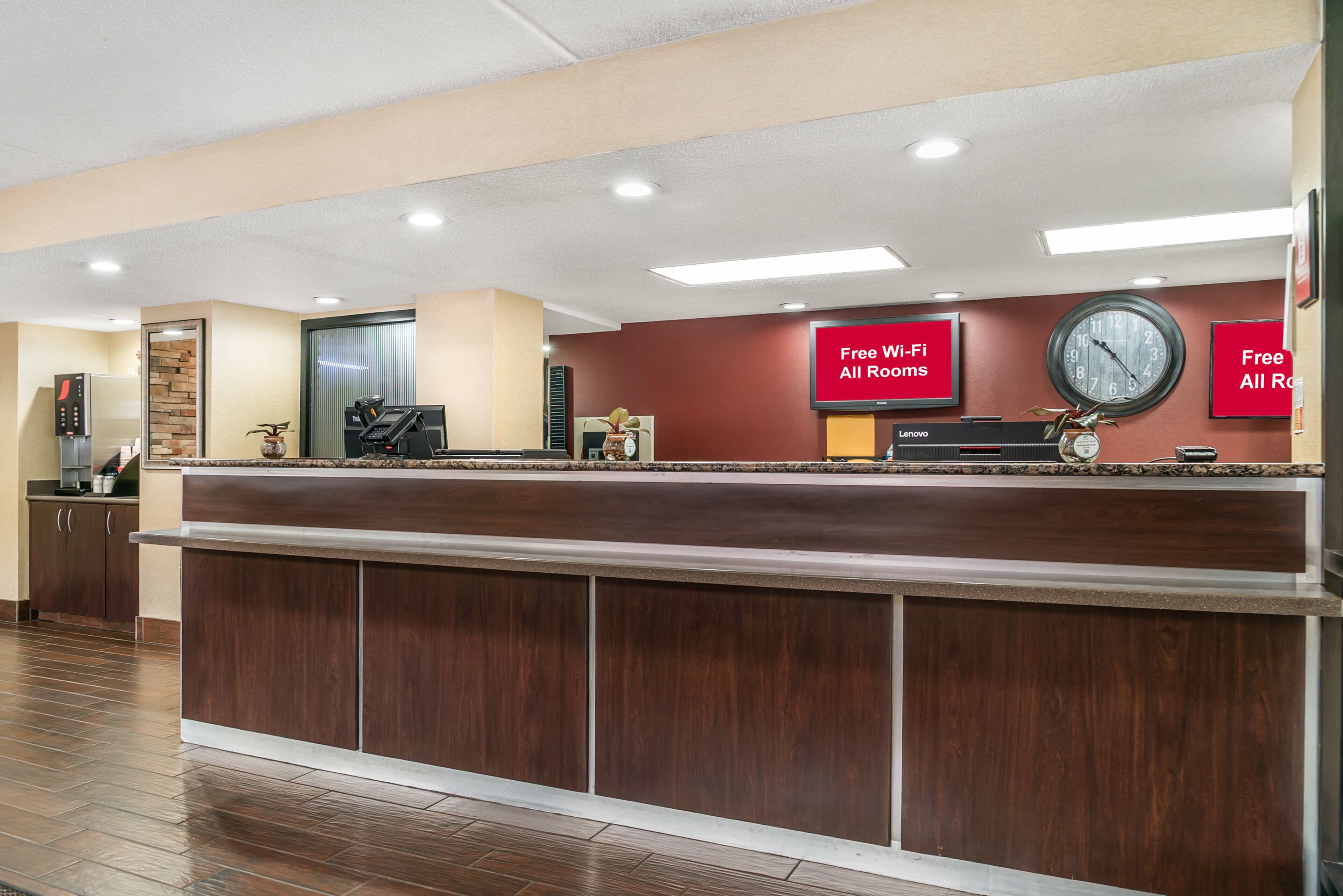 A hotel reception desk with a clock, a red sign indicating free Wi-Fi, and a wall-mounted clock.