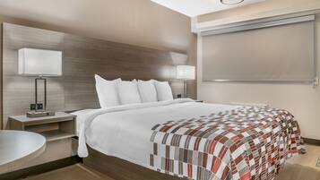 A modern hotel room with a large bed, two bedside tables with lamps, a built-in TV, and a round seating area.