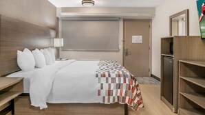 A hotel room with a bed, bedside table, lamp, wardrobe, and a door with a sign. - Red Roof Inn Detroit Metro Airport - Taylor (Taylor)