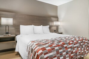 A hotel room with a large bed, two bedside tables, a nightstand, a wall-mounted lamp, and a bedside table lamp. - Red Roof Inn Detroit Metro Airport - Taylor (Taylor)